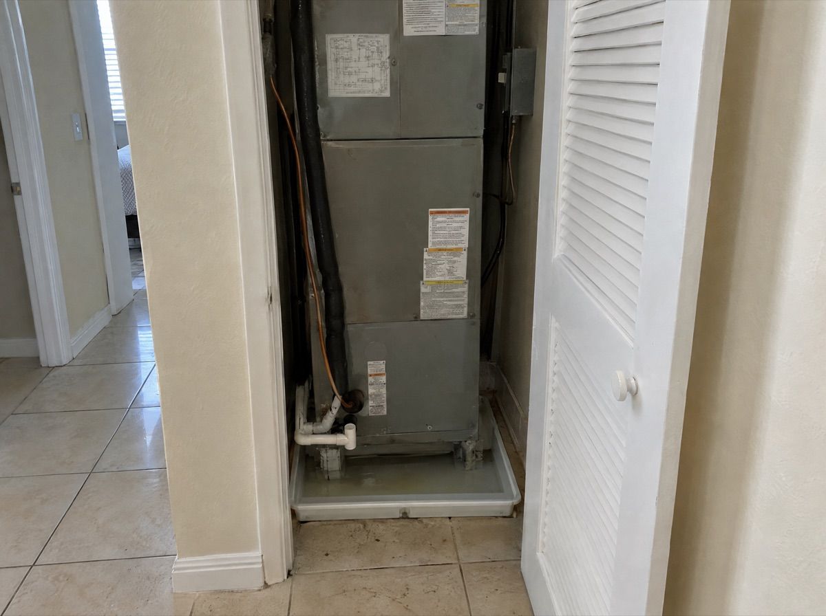 Air handler in a hallway closet with a little water in the drain pan below it.