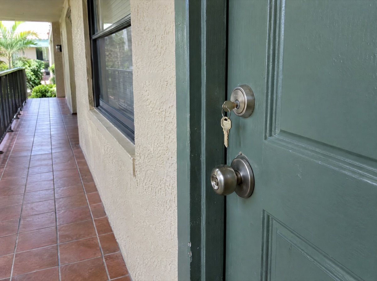 Apartment front door with keys in the lock, on an open-air walkway.