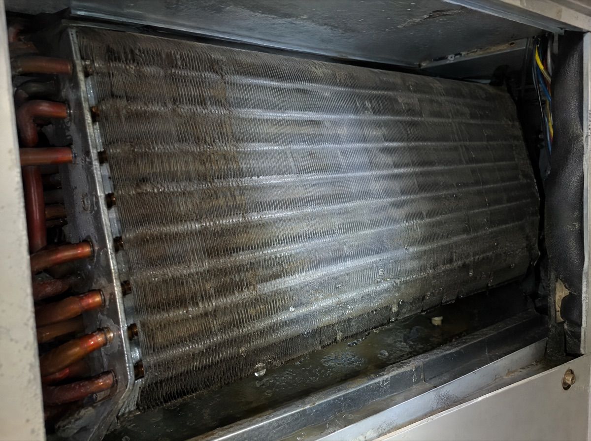 Close view of an air handler coil with dust and water droplets, lit by a flashlight.