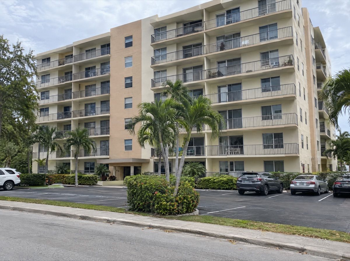 Mid-rise condominium building with balconies and palm trees.
