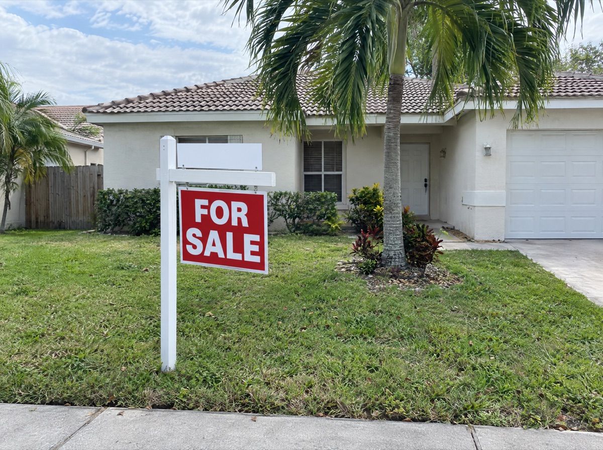 For sale sign on the front lawn of a stucco house.