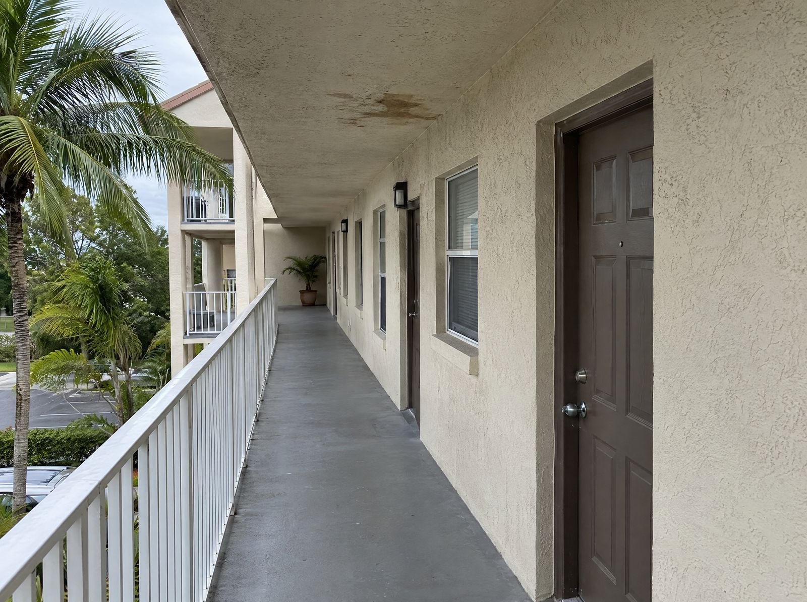 Open walkway of a condo building with unit doors and a stain on the walkway ceiling.