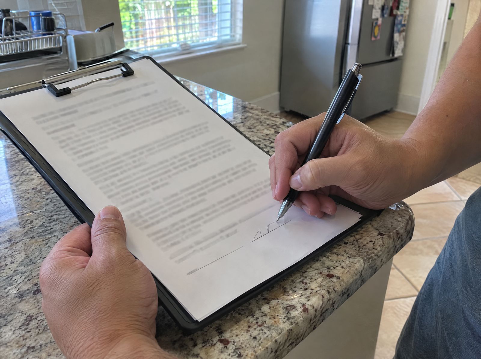 Hand signing a paper on a clipboard on a kitchen counter.