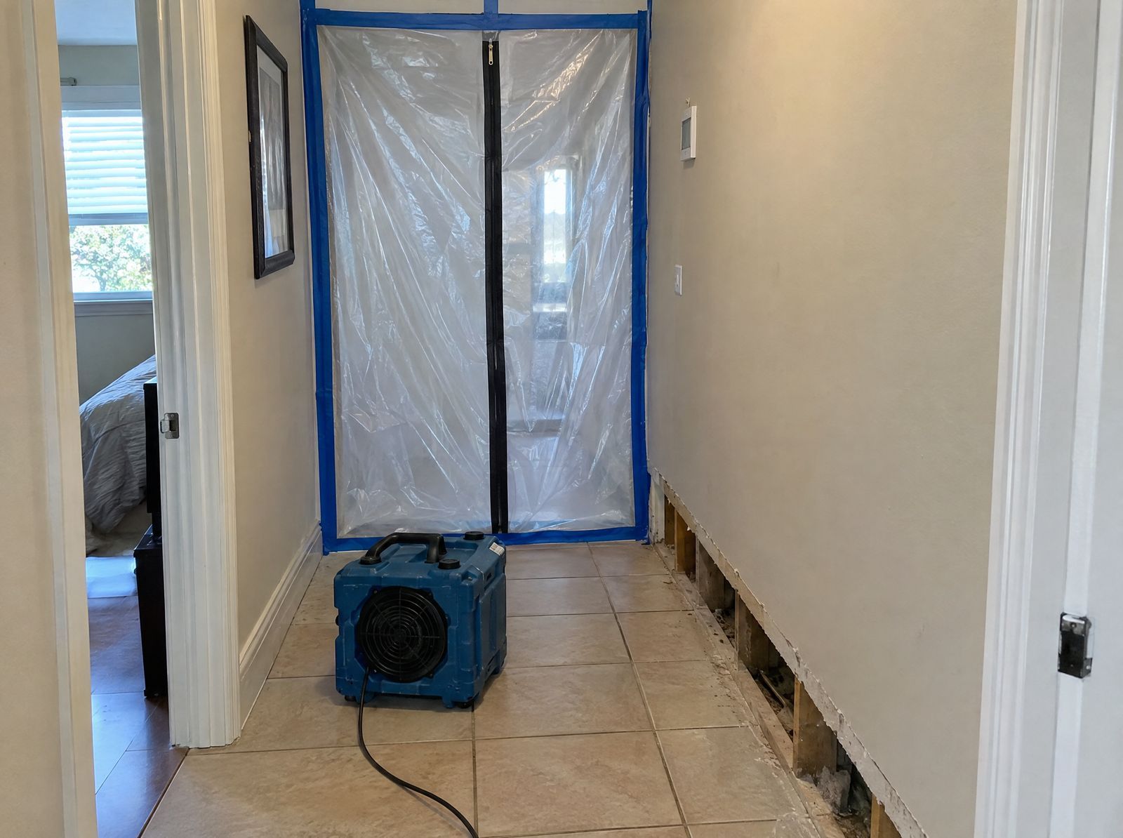 Hallway doorway sealed with clear plastic sheeting and a zipper, with a small air scrubber on the tile floor.
