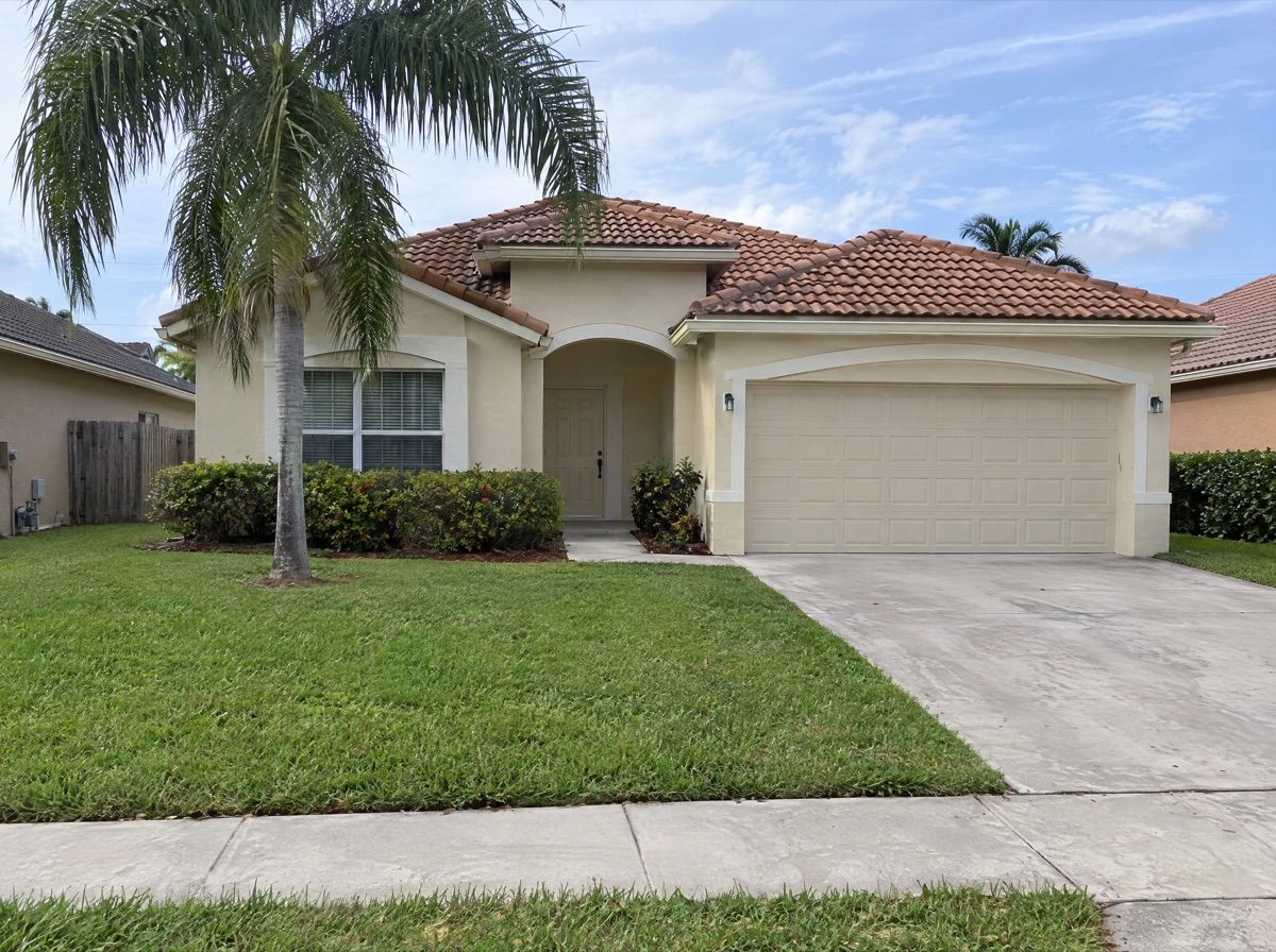 One-story stucco house with a tile roof, a lawn and a palm tree.