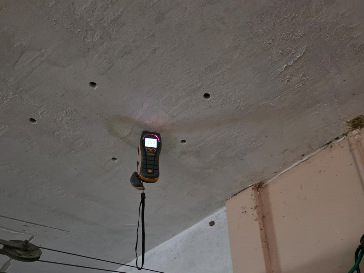 Moisture meter hanging against a stained concrete ceiling.