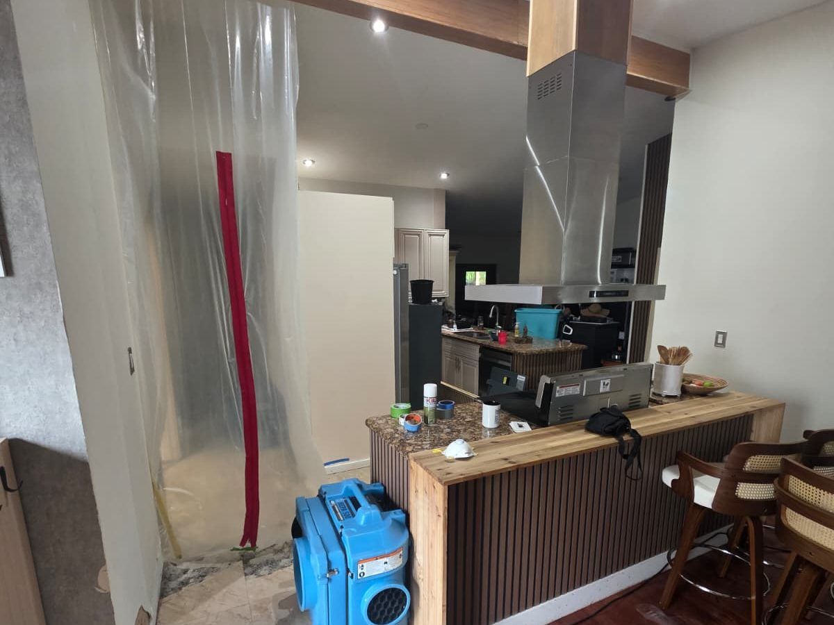 Plastic sheeting with a zipper door sealing a kitchen, with an air scrubber on the floor.