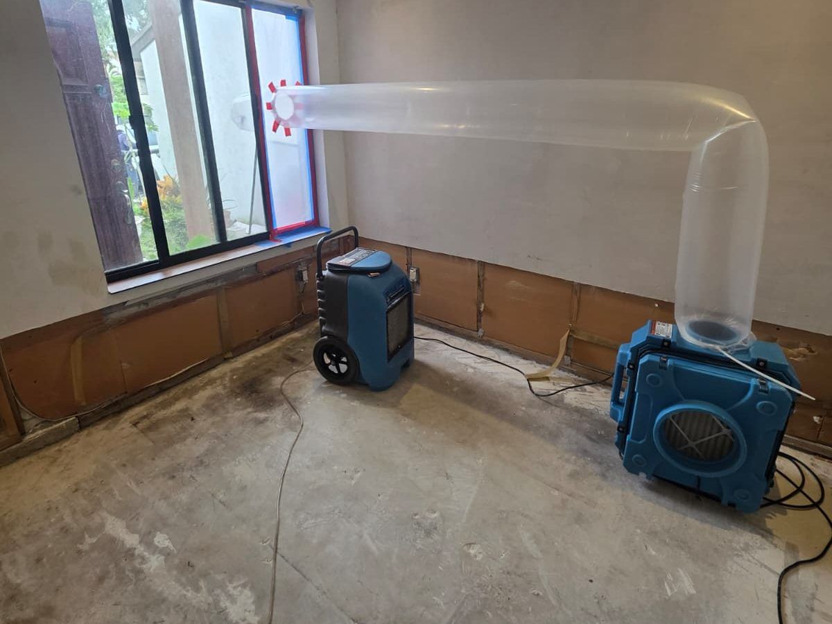 Dehumidifier and air scrubber with a clear duct set up in an empty room, with the lower wall opened.