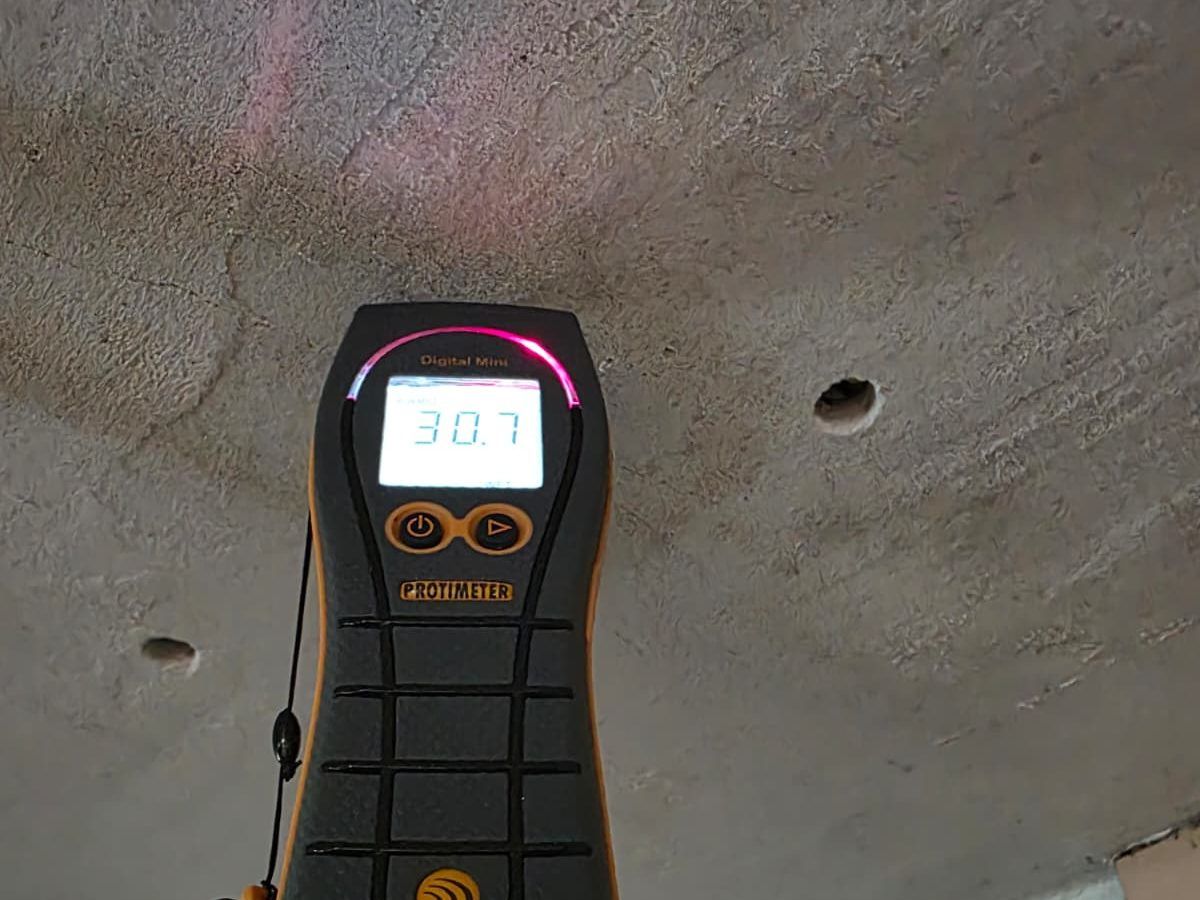 Close view of a moisture meter showing a reading on a concrete ceiling.