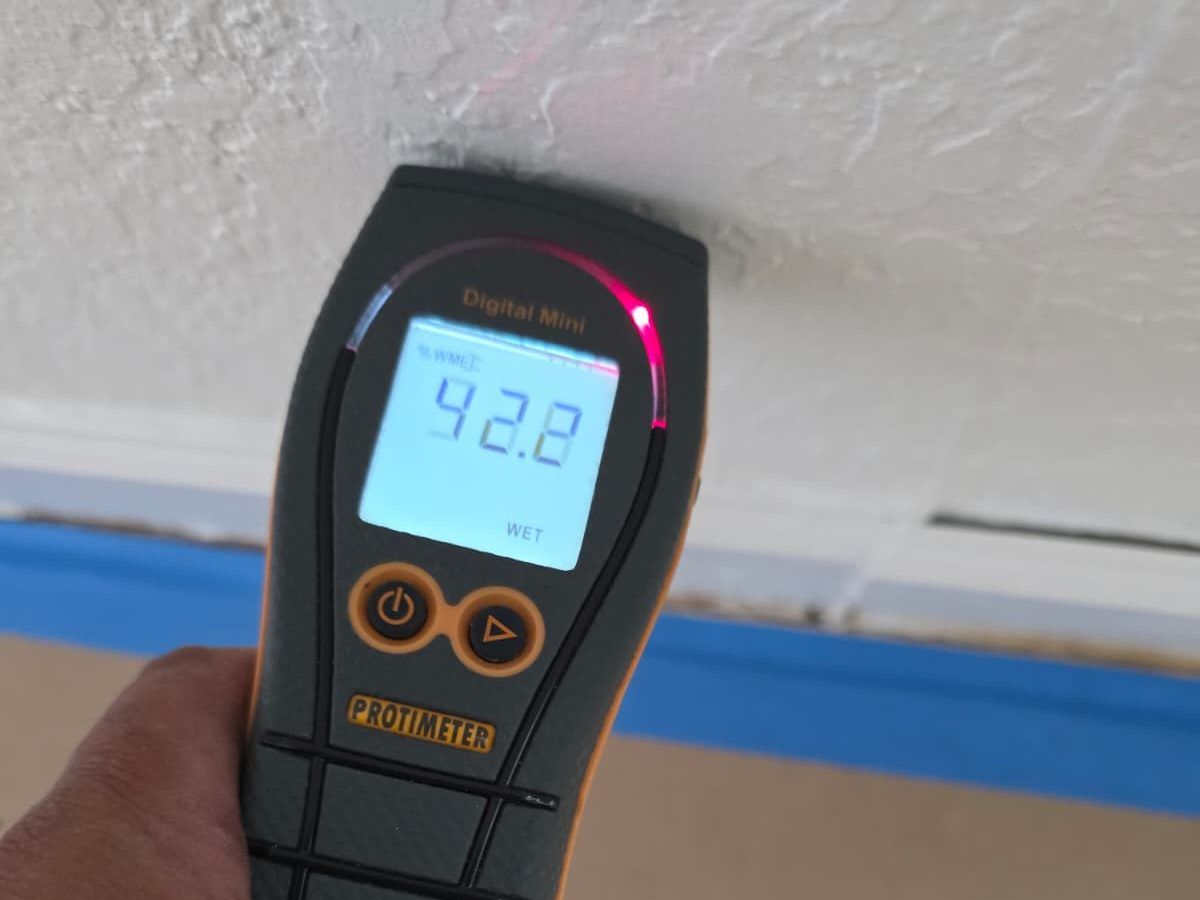 Hand holding a moisture meter against a ceiling; the display reads 92.2 and shows the word wet.