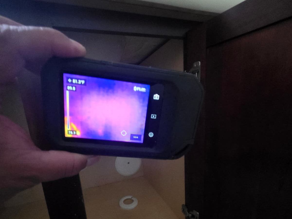 Thermal camera held inside an open cabinet, showing cooler and warmer areas on its screen.