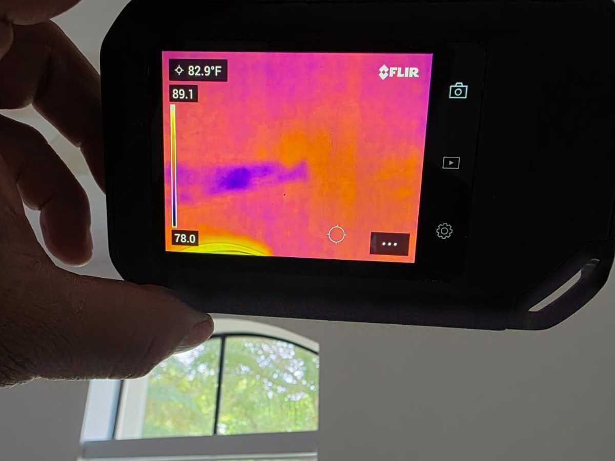 Thermal camera screen showing a cooler streak on a ceiling, held up near a window.