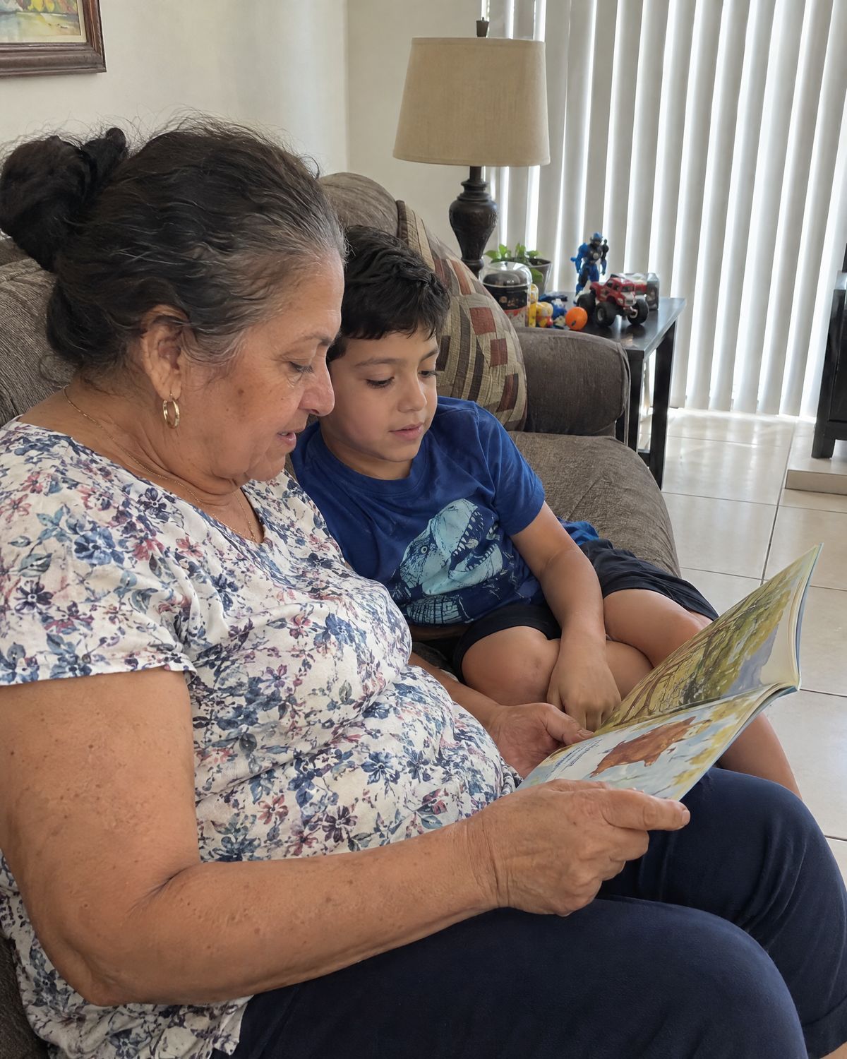 Mujer mayor leyéndole un libro ilustrado a un niño en un sofá.